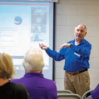 A presenter gestures beside a projection screen at a community gathering