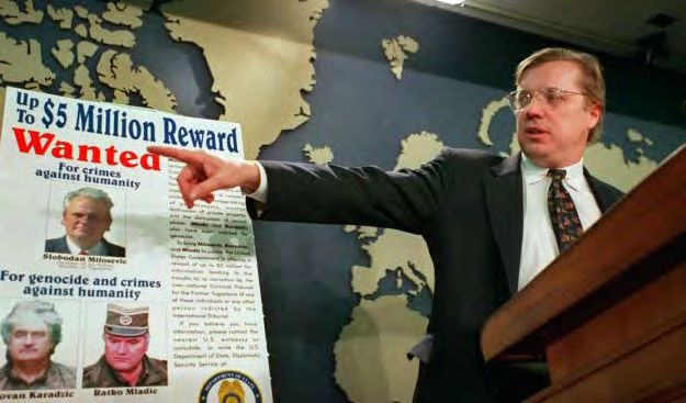 Official pointing to a Wanted poster offering a five million dollar reward for persons indicted for genocide and crimes against humanity