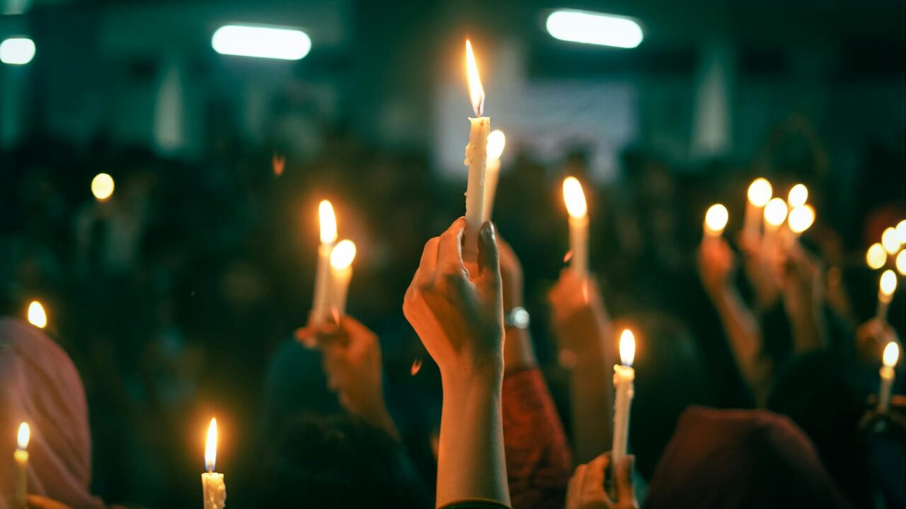 A group of people holding candles aloft in a public space, likely during a demonstration or vigil for human rights and u