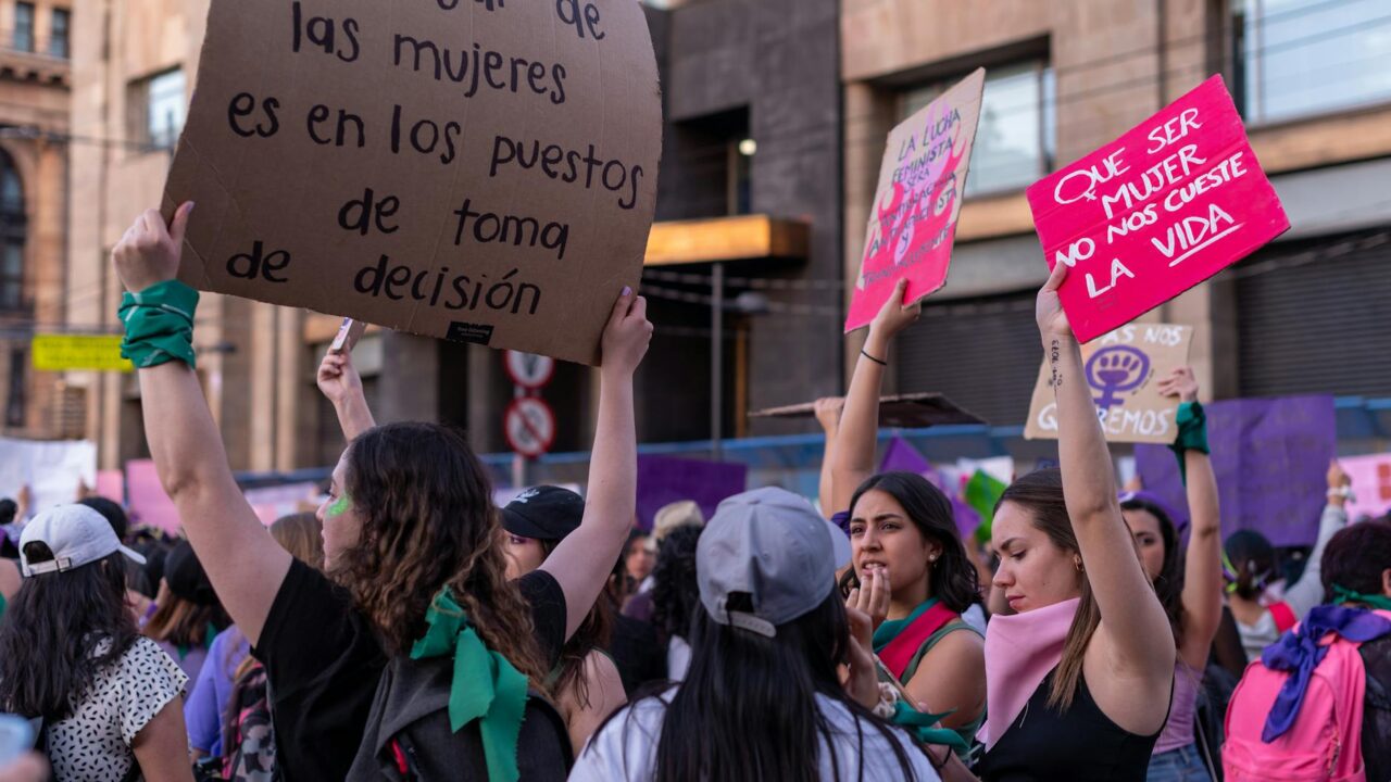 A group of women holding signs and banners during a protest, advocating for gender equality and women's rights.