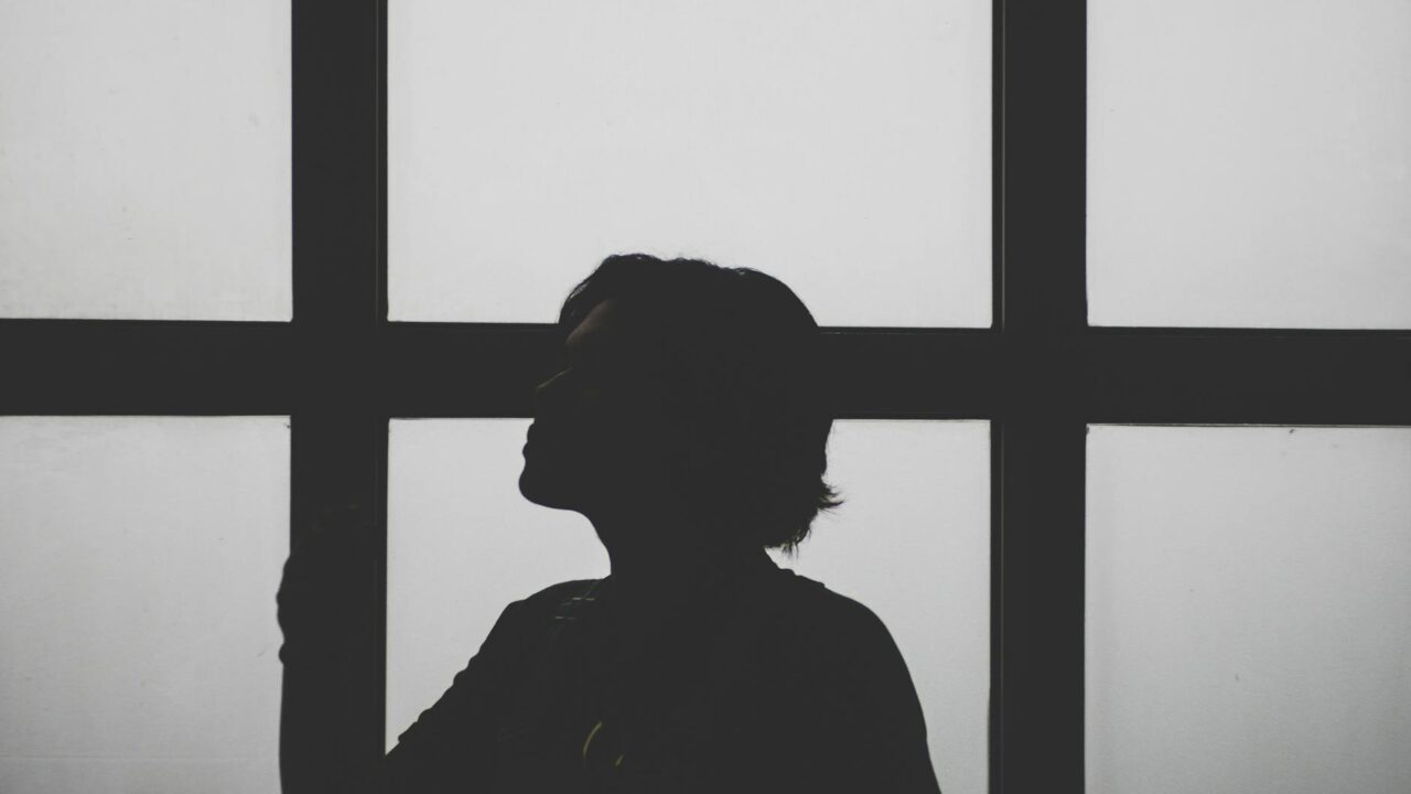 A person's silhouette against a window, reflecting on the glass.