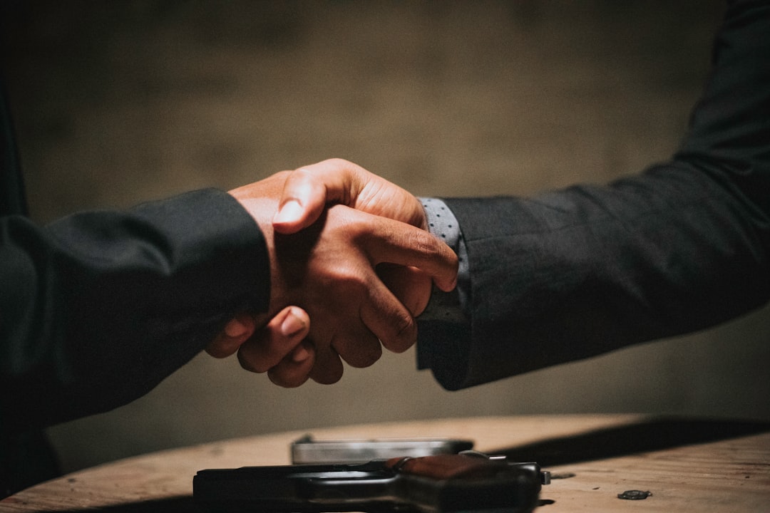 Two hands meeting in a handshake over a table.