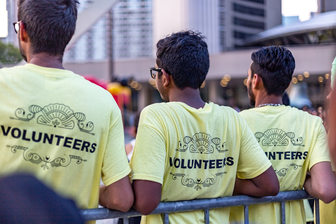 Volunteers wearing yellow shirts with 'VOLUNTEERS' printed on them, standing behind a barrier at an outdoor event in a c