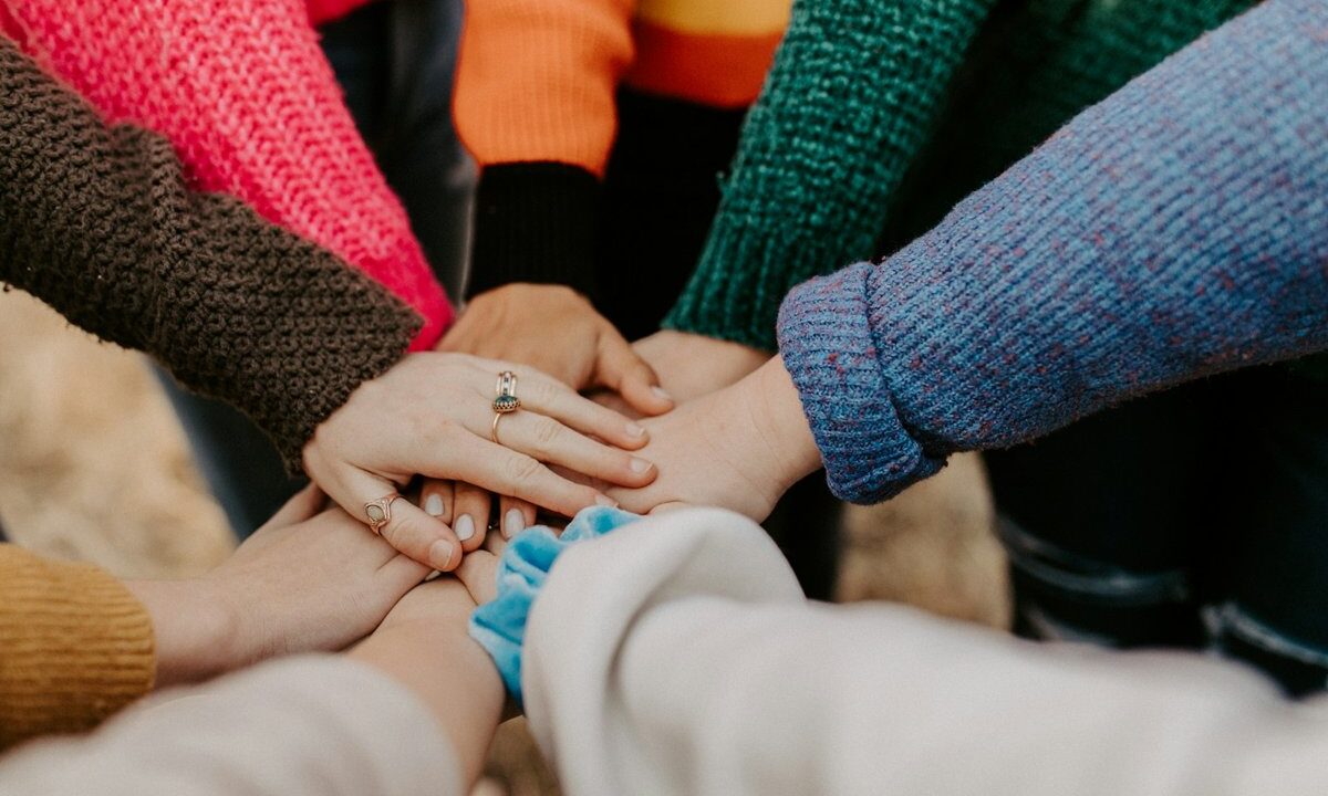 Many hands of different people stacked together in a circle, the universal gesture of shared belonging, for a poem that frames humanity as a common idea rather than a mere biological fact.