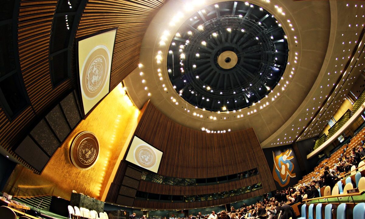 The United Nations General Assembly Hall in New York, its gold emblem and domed ceiling above a seated assembly, the universal image of a congress of nations for a World Federalist Movement national congress keynote.