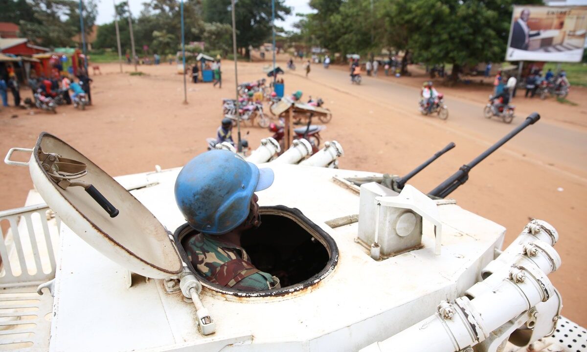 A United Nations peacekeeper (blue helmet) in a white UN armored vehicle watching over a town street with civilians, a direct picture of protection of civilians, the heart of the Responsibility to Protect.