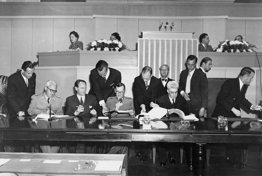 The 1949 signing ceremony of the Geneva Conventions, delegates seated at the table signing the treaty texts, the founding moment of modern international humanitarian law.