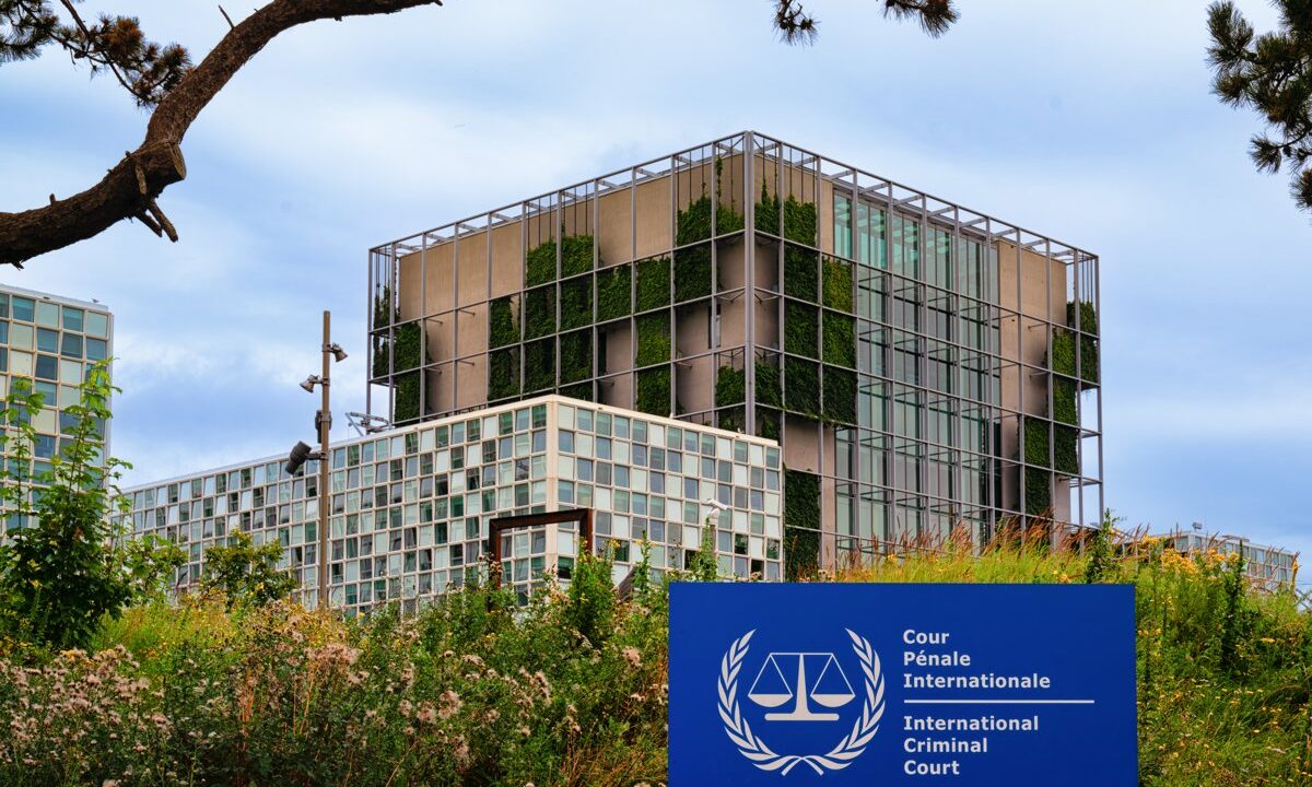 The cube tower of the International Criminal Court building in The Hague rising above greenery, with the ICC sign in the lower corner, a distinct architectural view of the court.