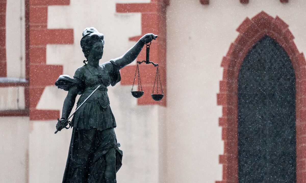 A monumental Lady Justice statue holding aloft a prominent set of scales against a historic facade in falling snow, a clear symbol of justice and the rule of law for an essay on legal obligations in the face of atrocity crimes.