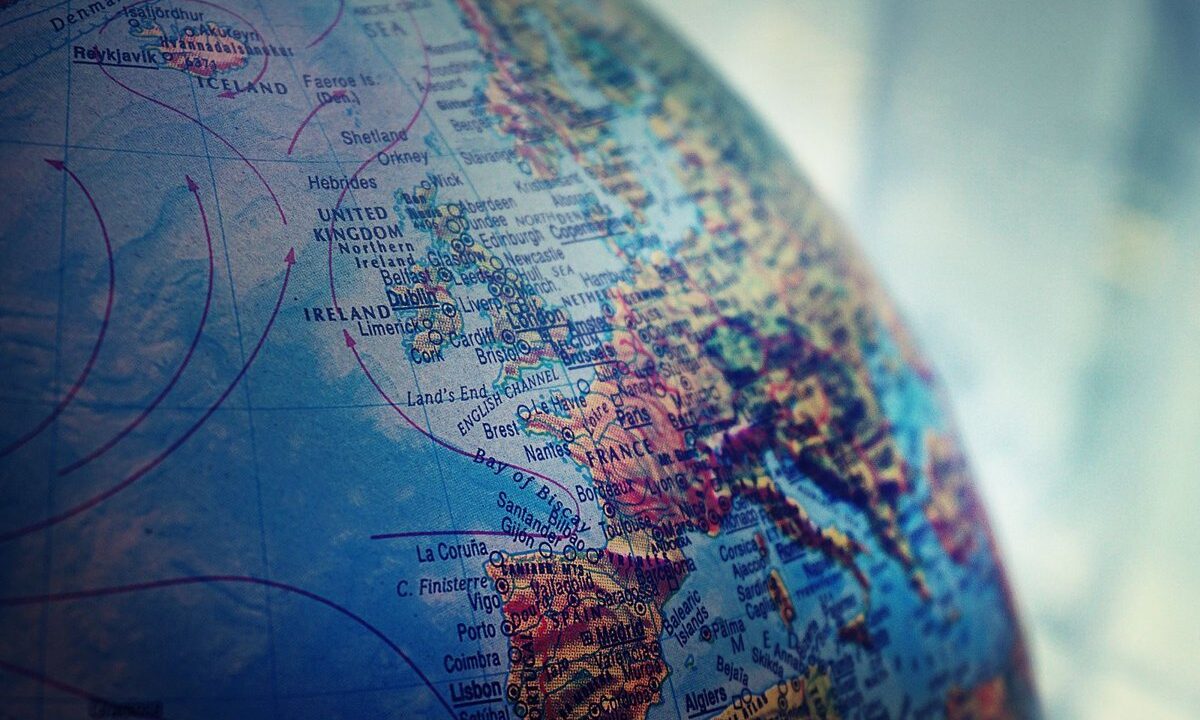 A soft-focus close-up of a classic world globe across Western Europe and the Atlantic, with old shipping and wind arrows: a dignified, tactile image of the world as the thing being built into a federation.