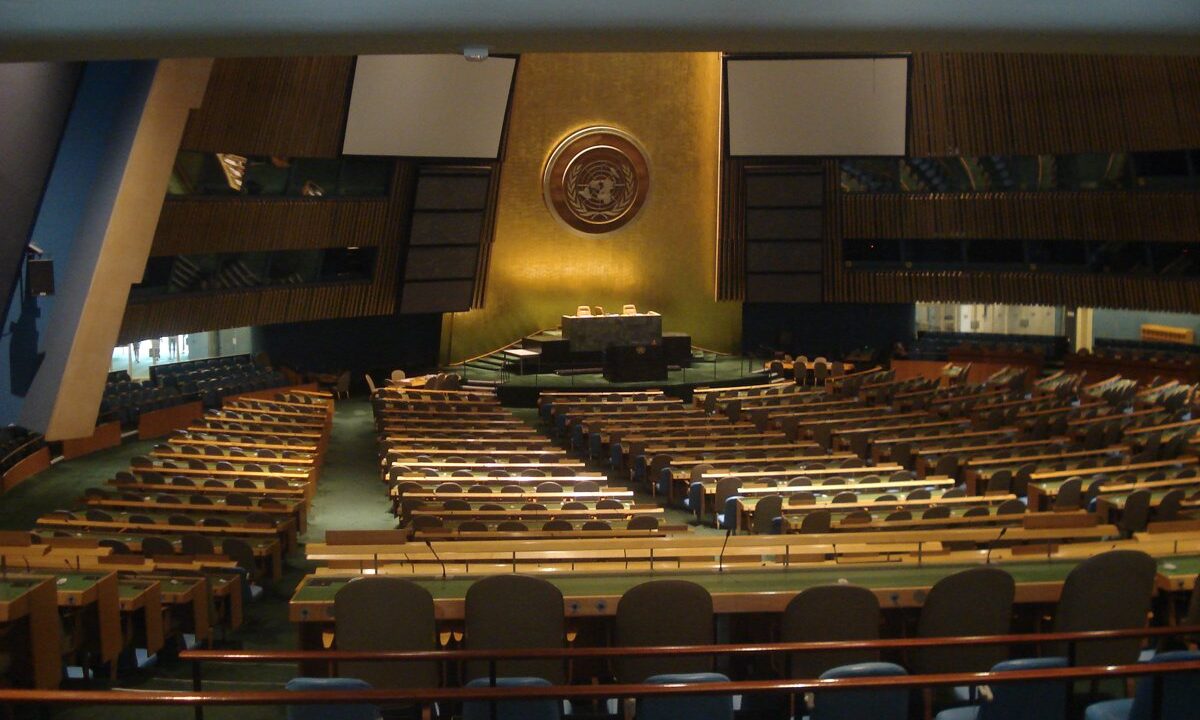 The empty United Nations General Assembly hall viewed head on toward the gold emblem and the rostrum, the podium from which the world addresses itself.