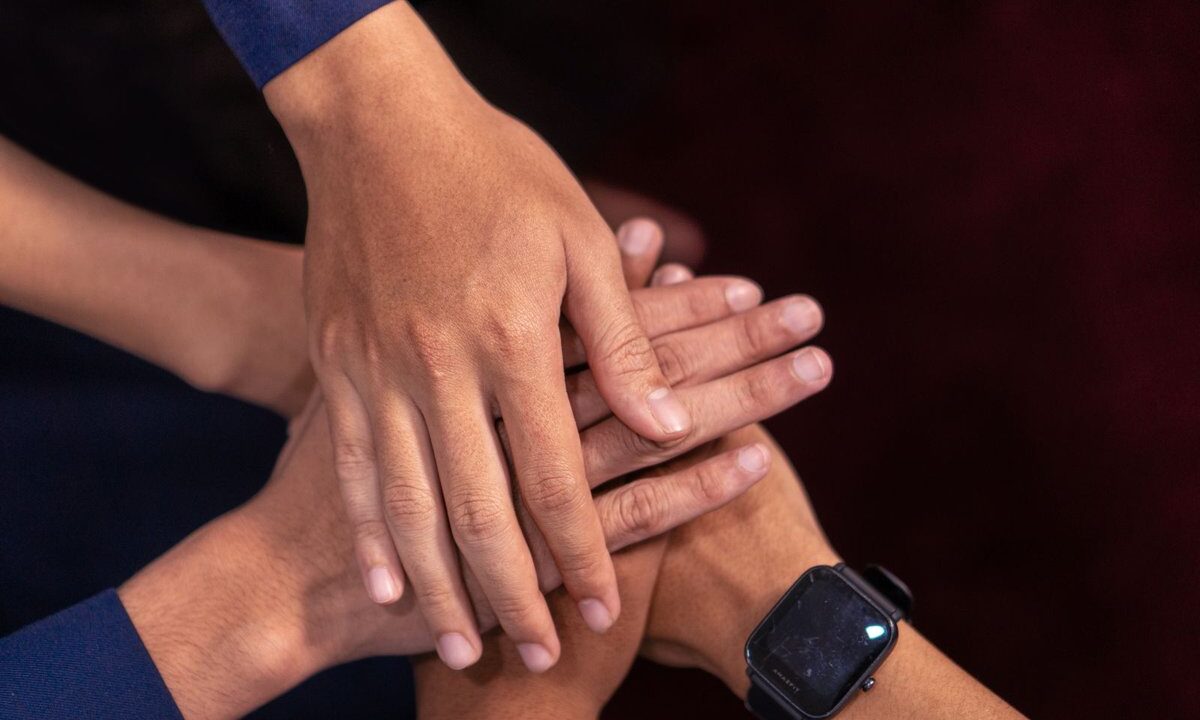 Many diverse hands of different people stacked together in a gesture of unity against a warm dark background: a conceptual image of shared humanity and a common duty to one another.