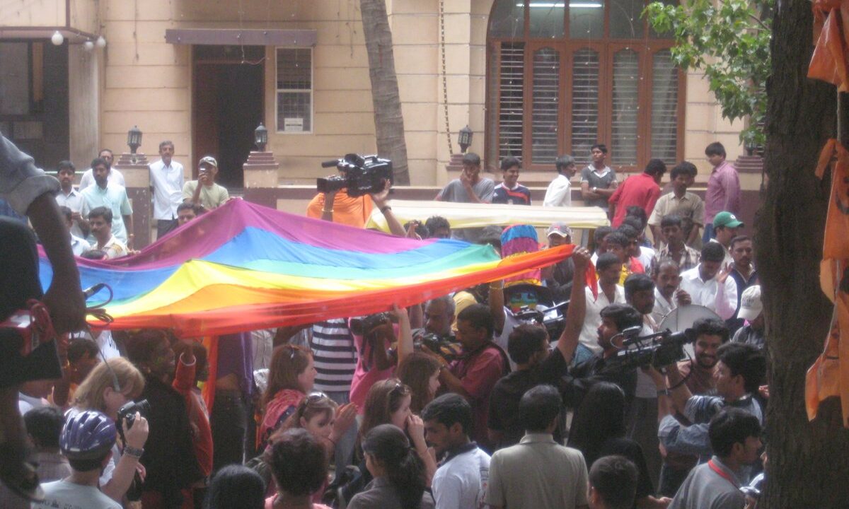 A large rainbow Pride flag held aloft by a crowd at the Bangalore Gay Pride parade, an international image of the LGBTQI+ rights the article argues a world federation should protect as universal human rights.