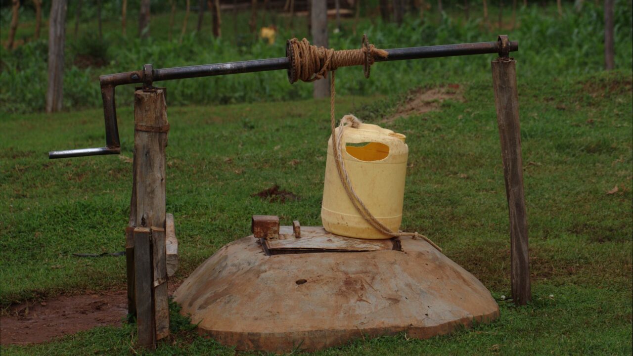 A simple water pump with a yellow container attached, likely for agricultural use in a rural setting.