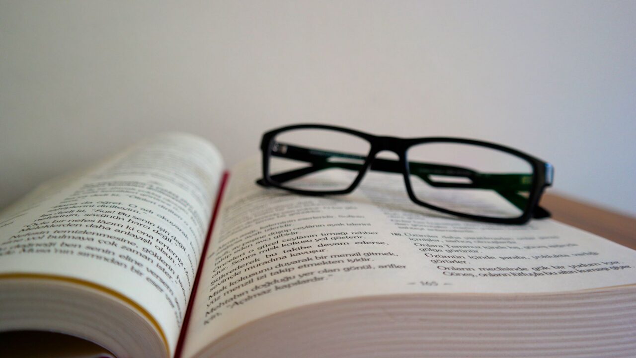 A pair of glasses resting on a book, suggesting a moment of study or intellectual pursuit.