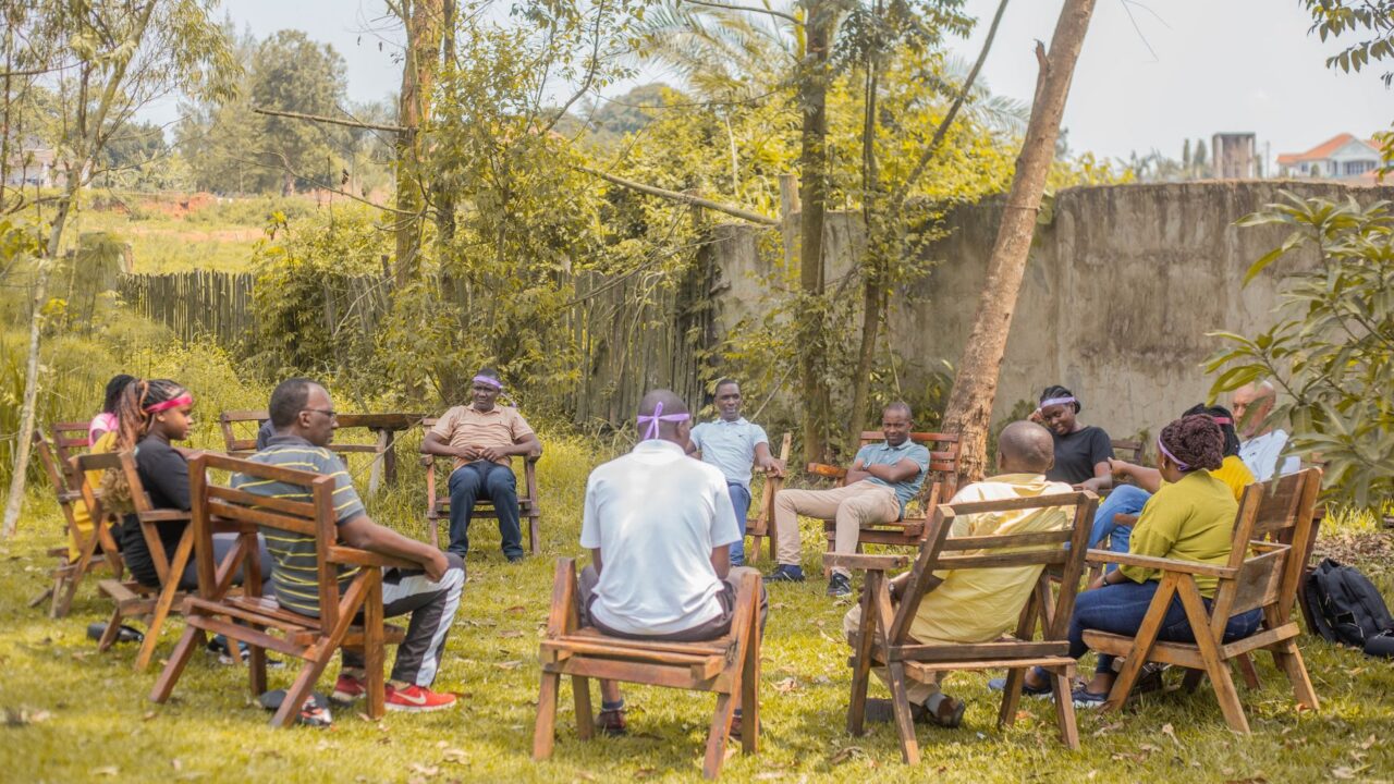 A group of people sitting in lawn chairs, engaged in conversation in a grassy area with trees in the background.