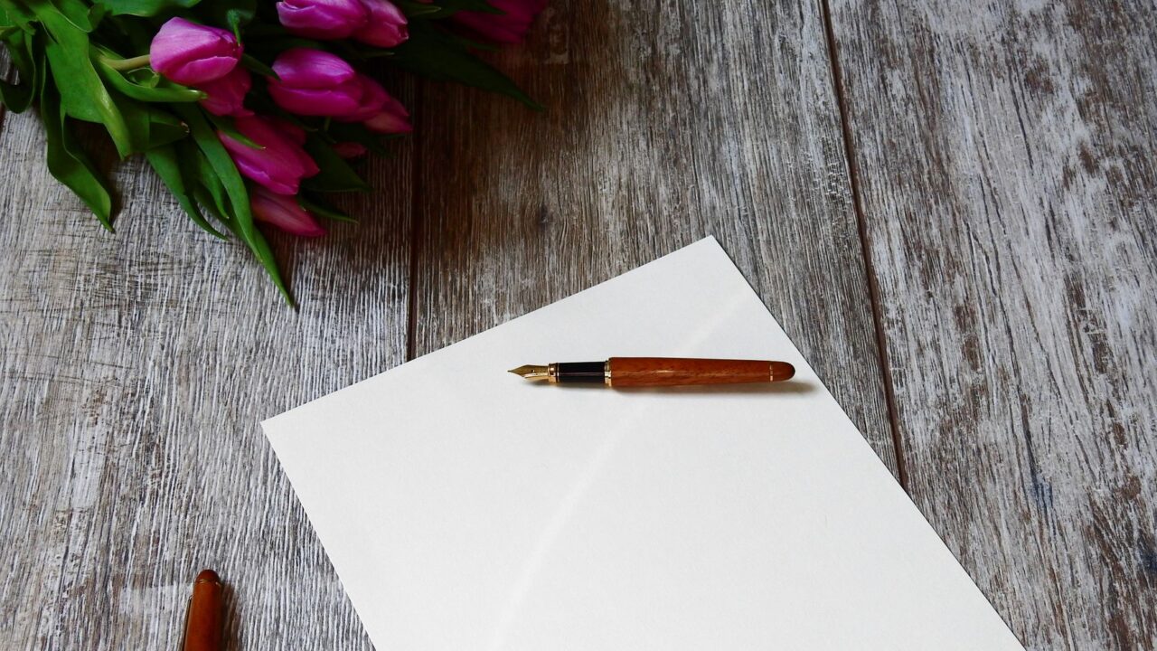 A blank card with a pen on a wooden table, surrounded by a bouquet of flowers.