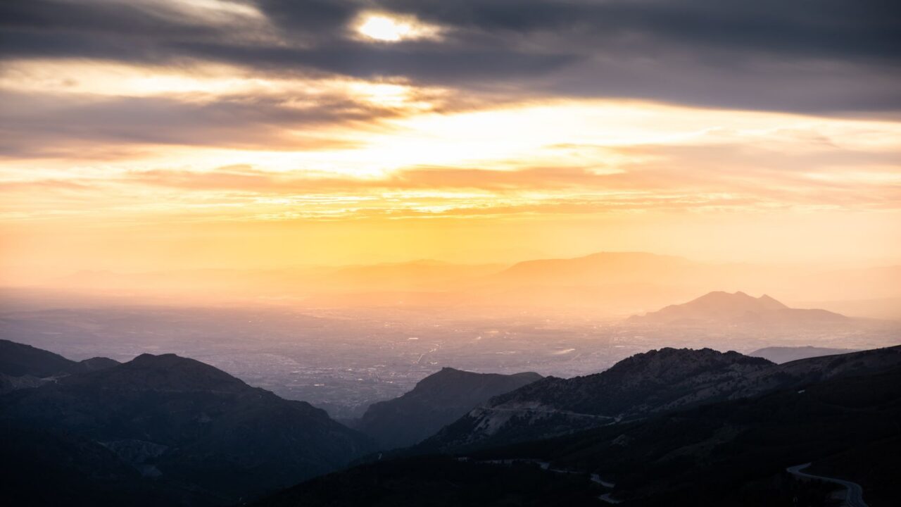 Sunset over a mountainous landscape with clouds and mist.