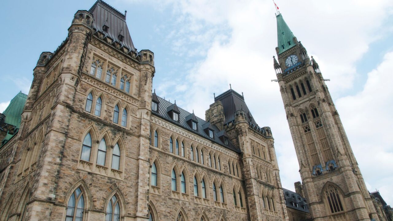 The image shows the iconic Parliament Buildings in Ottawa, Canada, with the Peace Tower and the clock tower prominently