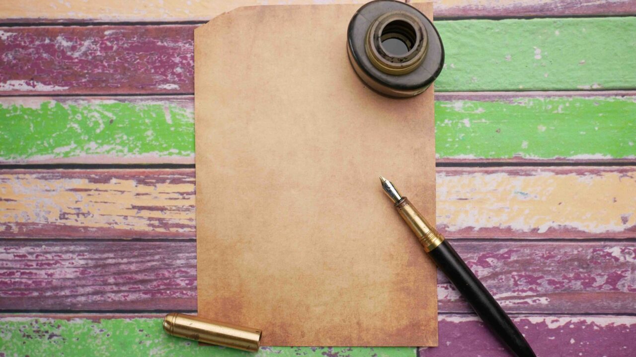 A vintage paper with a pen and ink on a colorful wooden table.