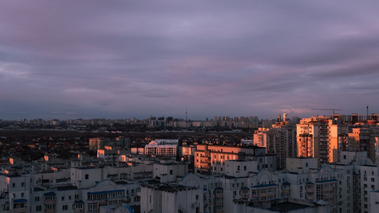A city skyline at dusk, with buildings illuminated by the warm glow of the setting sun.