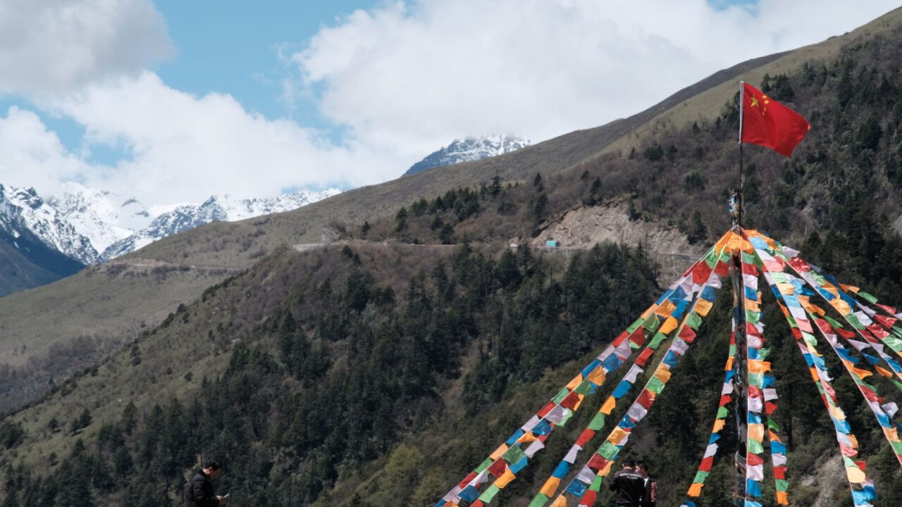 A colorful kite with a red flag atop a mountain, set against a clear sky.