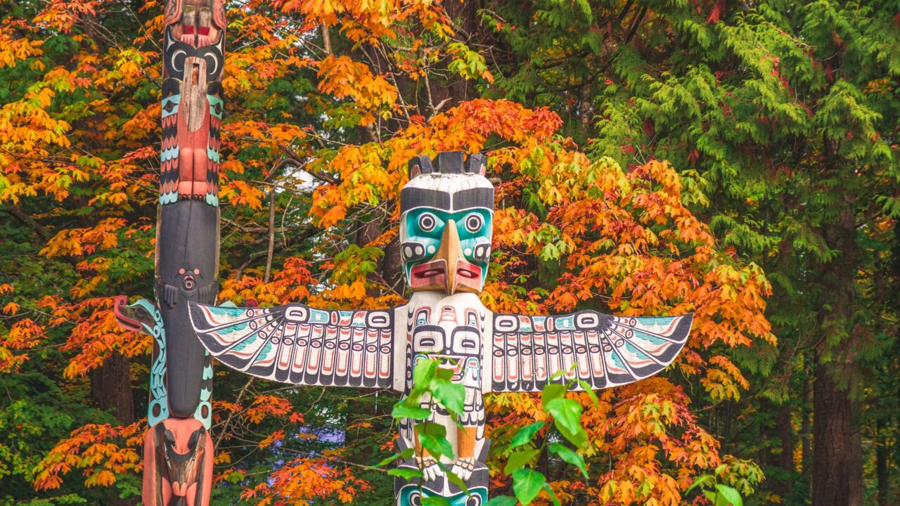 Carved and painted totem poles among autumn trees.