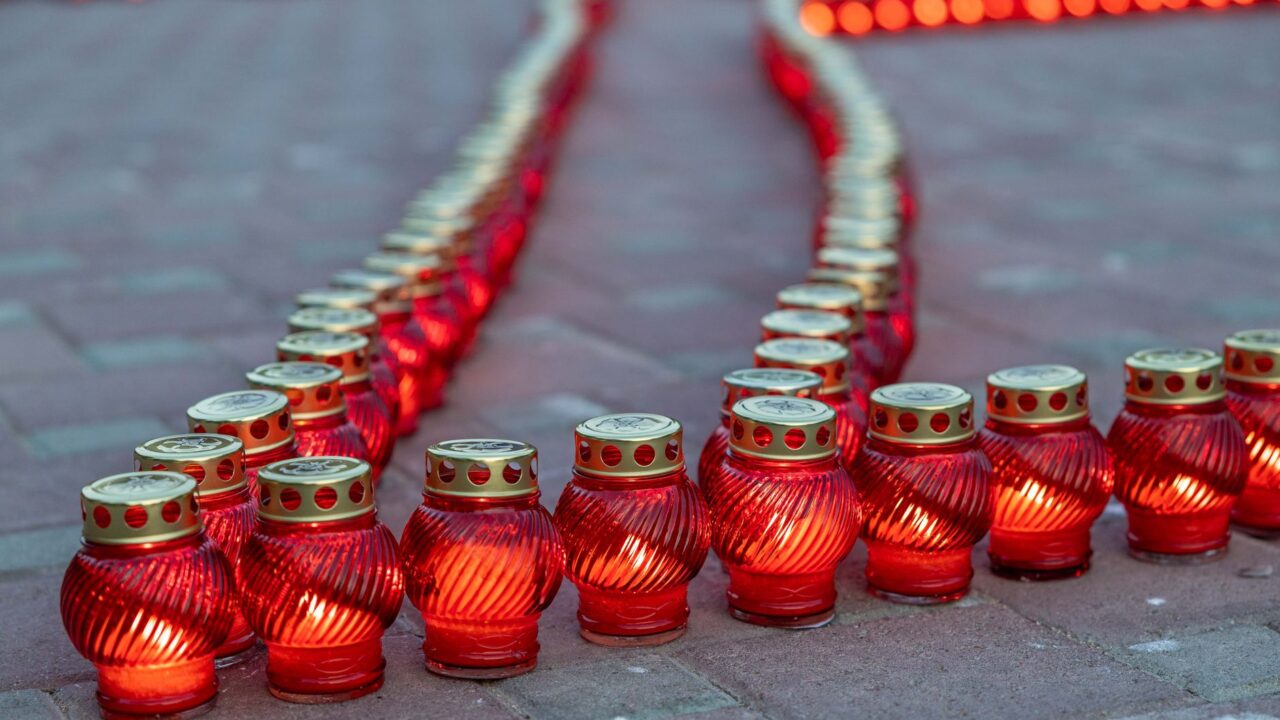 Rows of red memorial candles lit on a paved square.