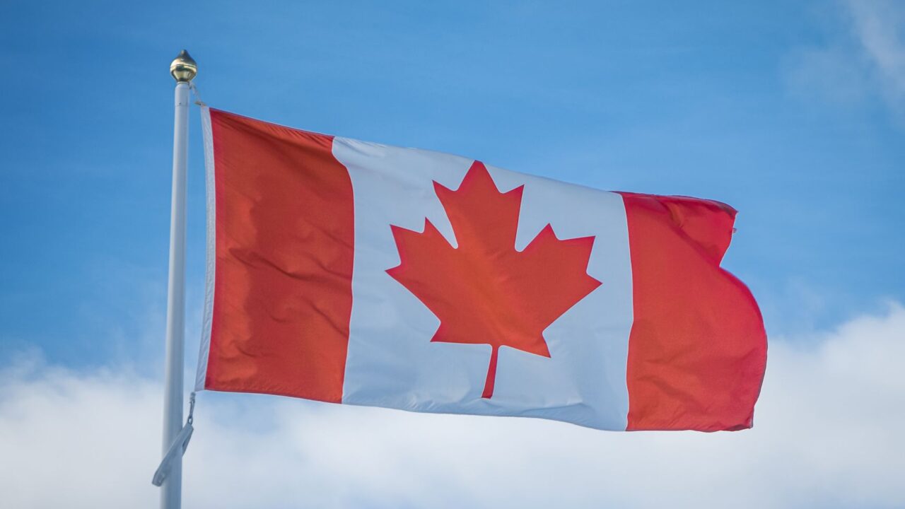 The Canadian flag flying from a pole against the sky.