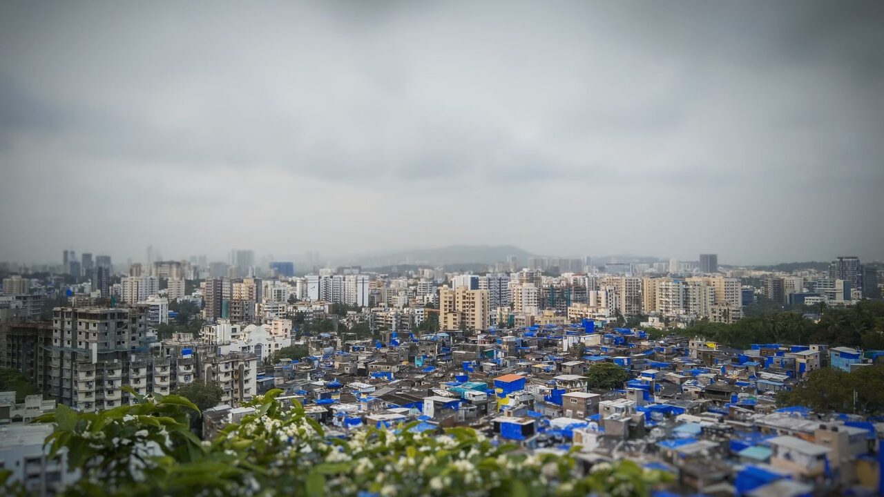 An informal settlement with blue tarpaulin roofs below high rise towers.