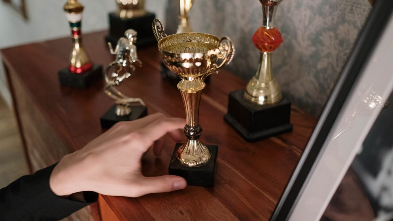 A hand setting a gold trophy among others on a wooden table.