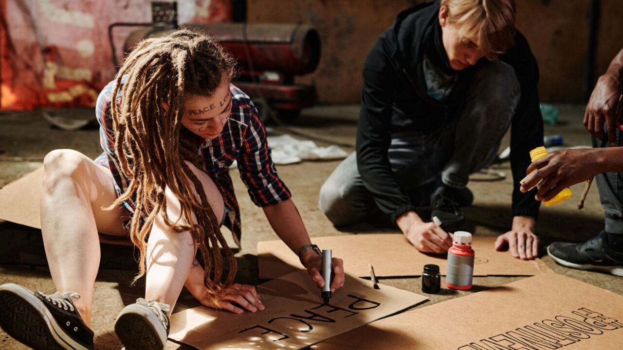 A group of people sitting on the ground, working on a sign or banner, with a focus on activism and social change.