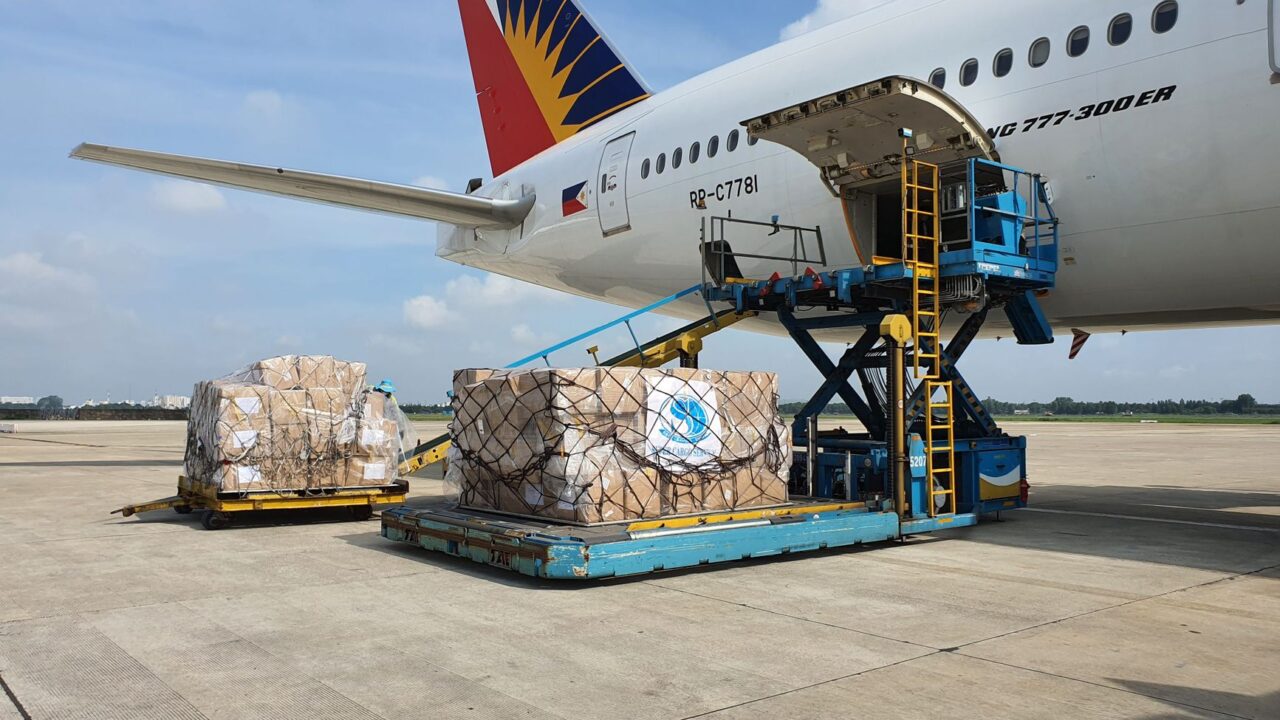 A large commercial airplane parked at an airport with its cargo hold open, being loaded with packages.