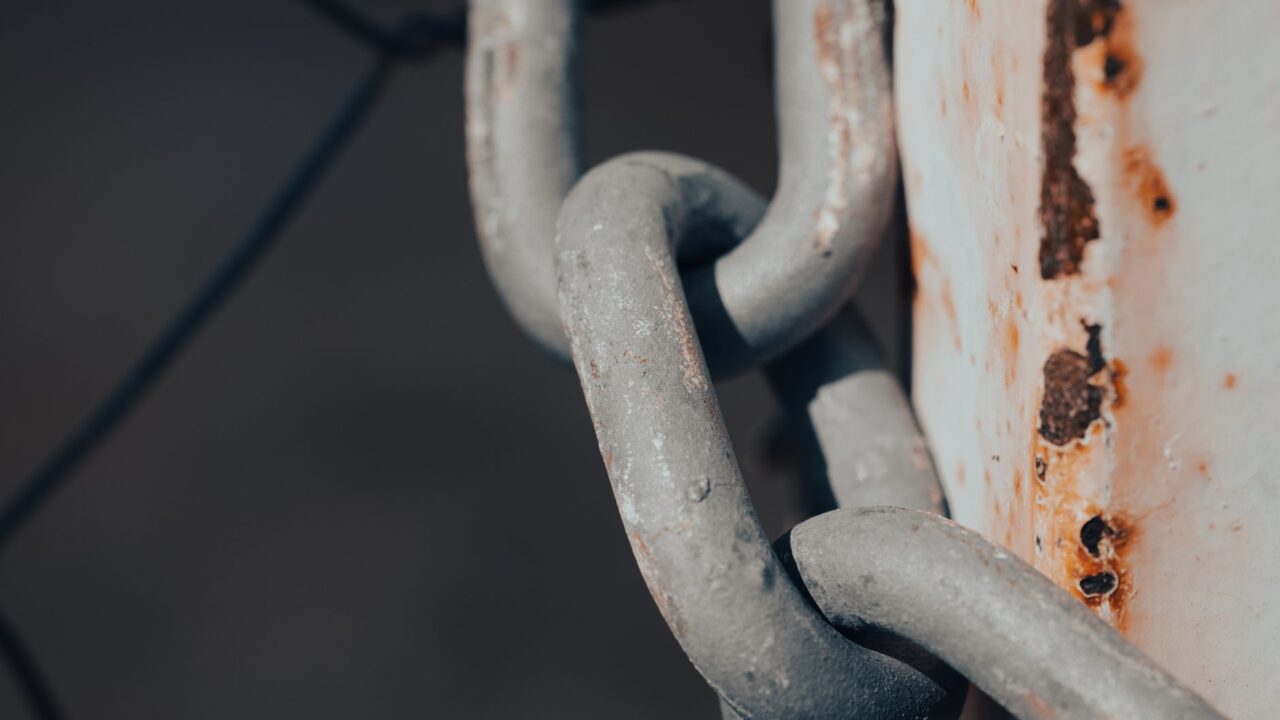 A close-up of a rusted metal chain and padlock, suggesting security or confinement.