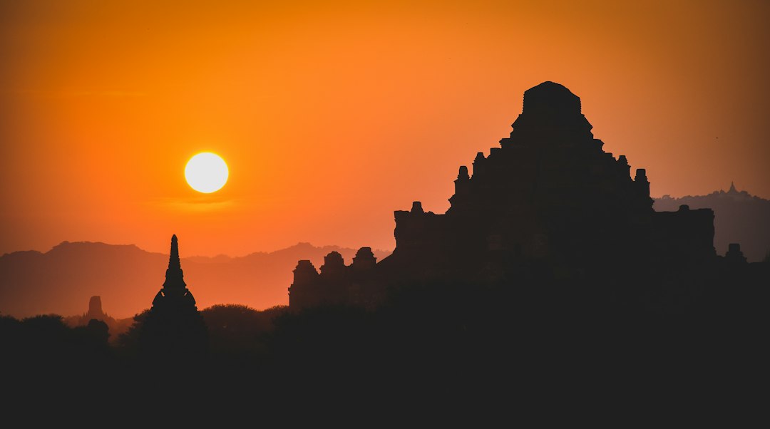 The sun is setting over a temple complex, casting a warm glow on the ancient architecture.