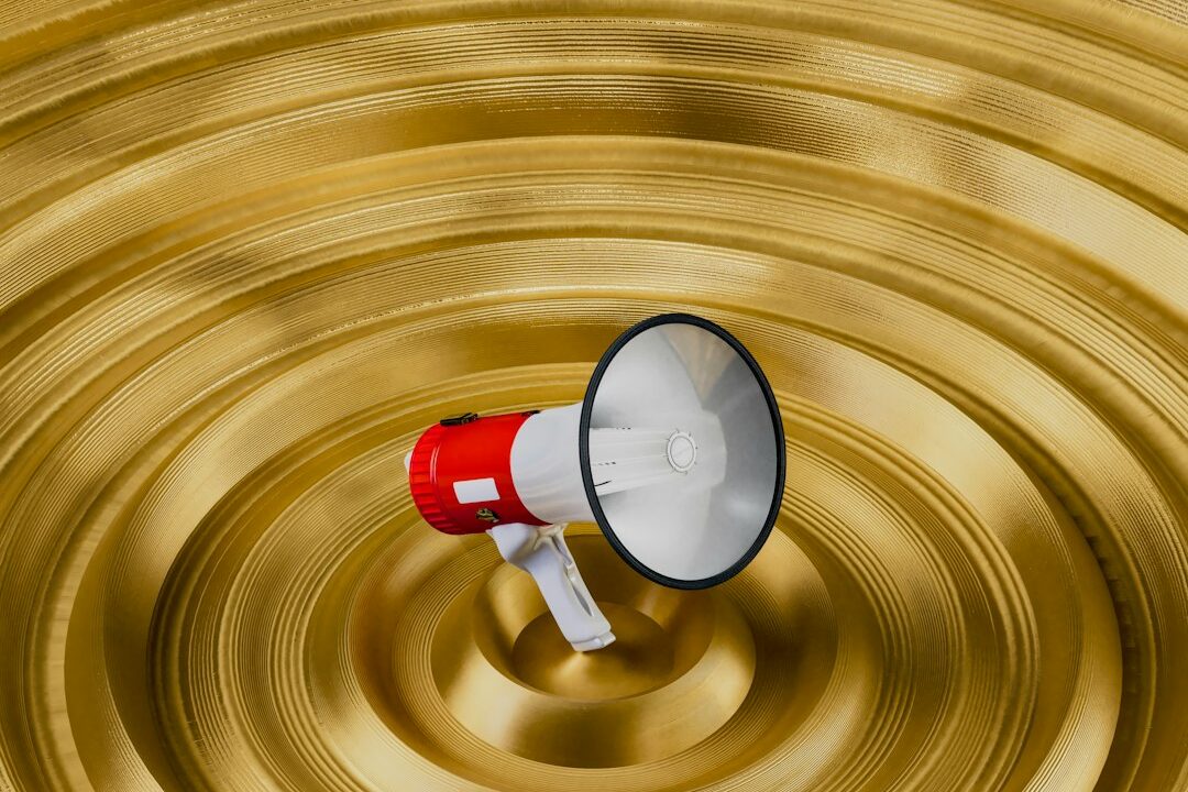 A red megaphone on a golden background with concentric circles, possibly representing sound waves or amplification.
