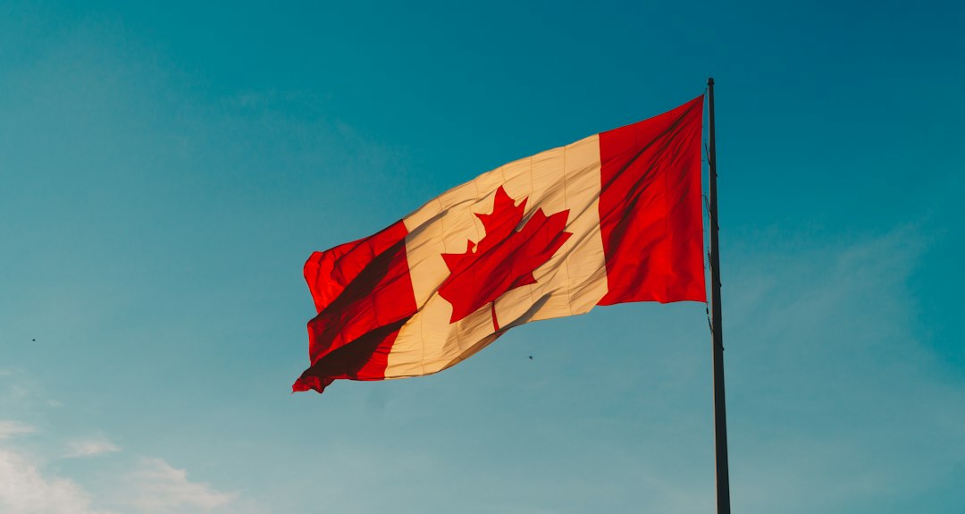 A Canadian flag flying against a blue green sky.