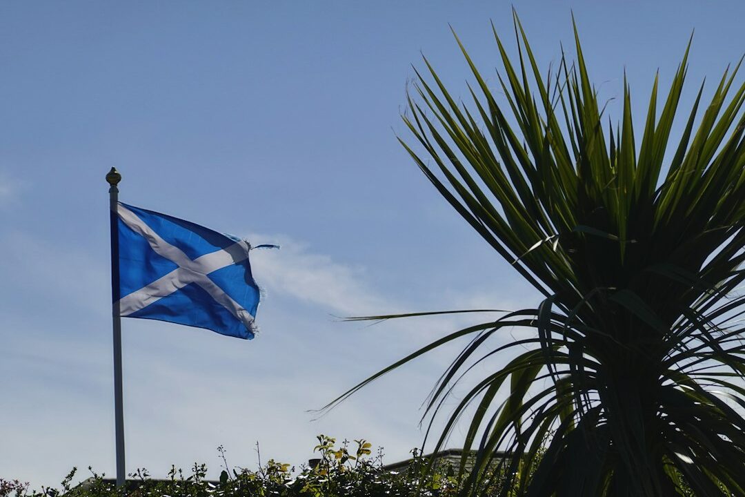 A blue flag with a white cross, symbolizing Scottish nationalism, flying on a pole in the sunlight.