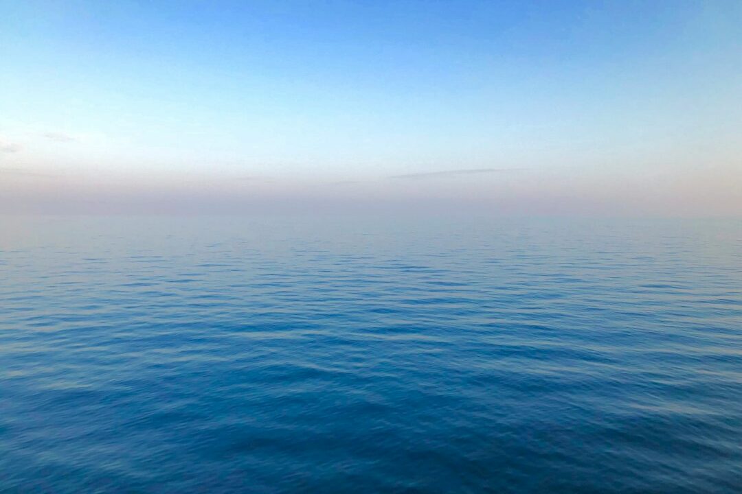 A serene ocean horizon at sunset, with the sky transitioning from blue to orange.